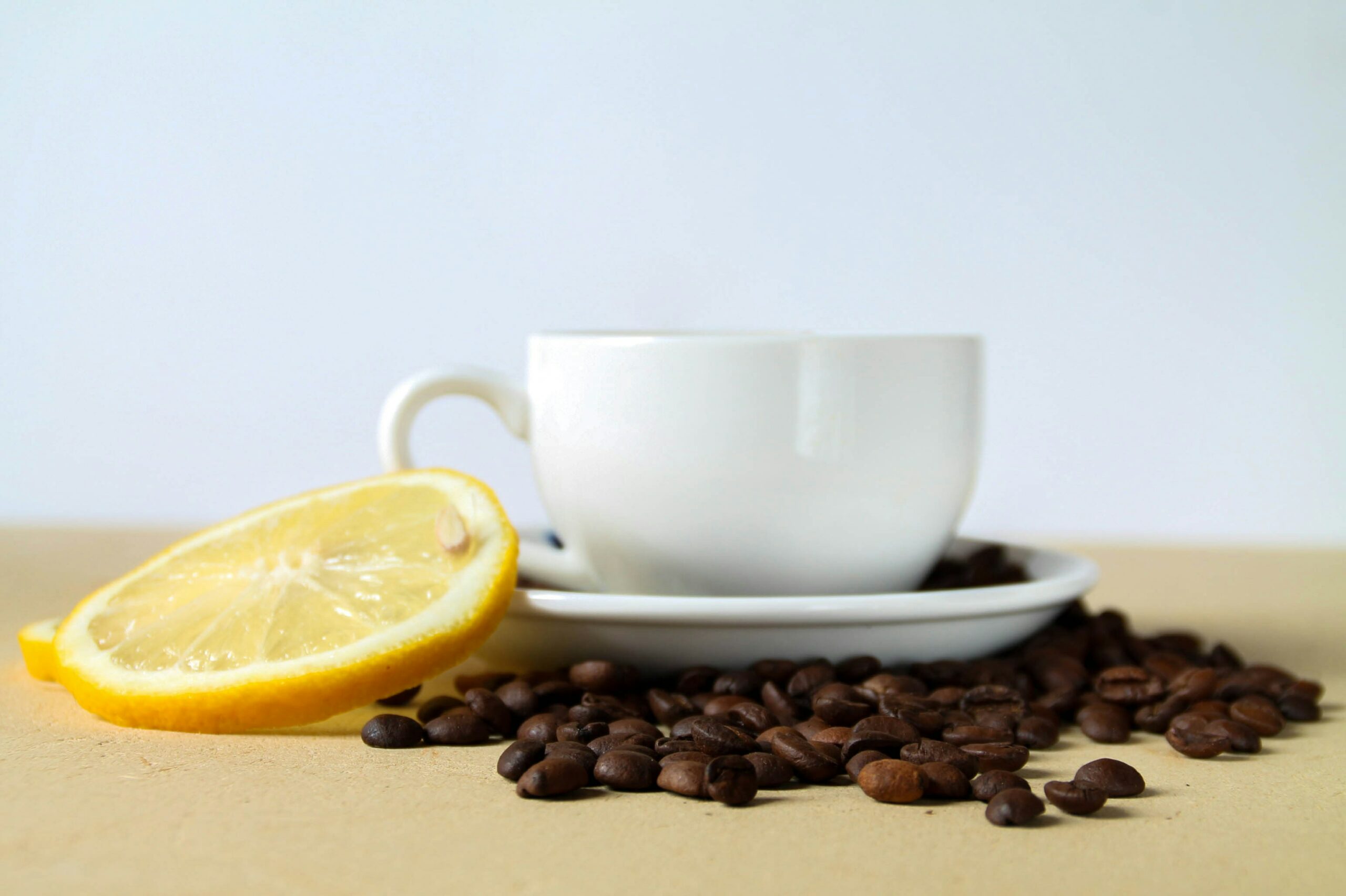 Eine Tasse Kaffee umgeben von Kaffeebohnen und eine Zitronenscheibe, die auf der Tasse lehnt.